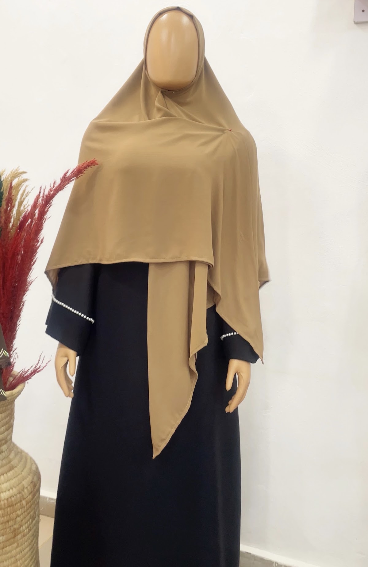 Modeste camel triangle wrap draped over black abaya with pearl cuffs